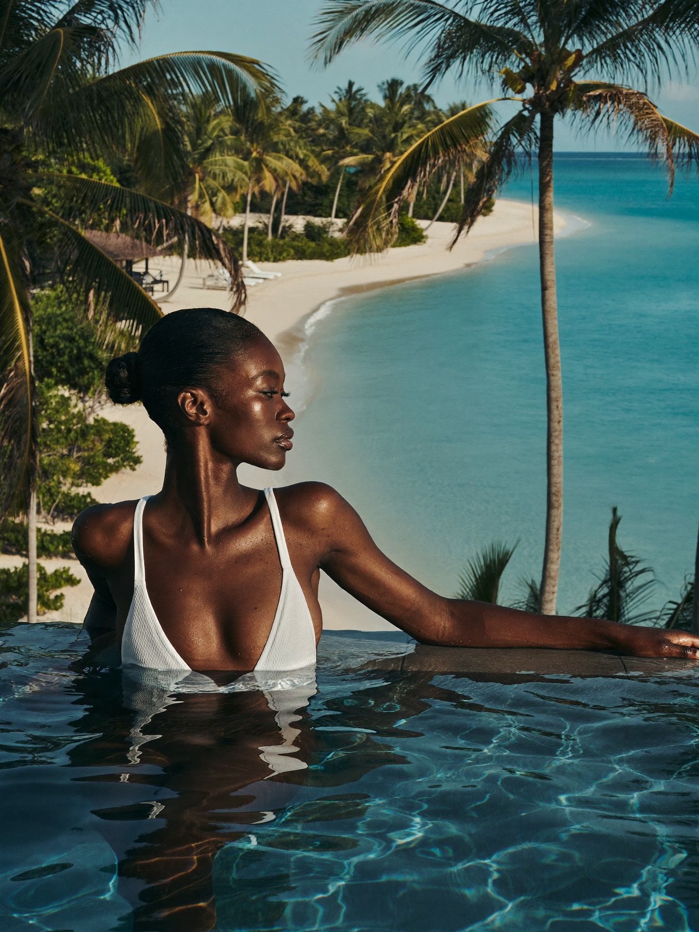 A woman relaxing at the edge of an infinity pool above the turquoise sea
